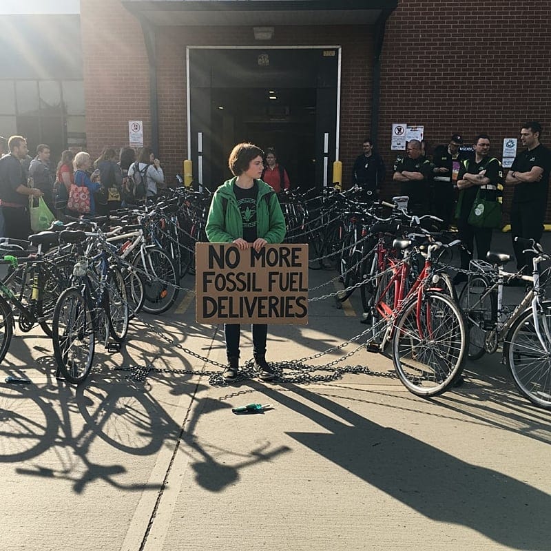 Police officers attempting to remove locked bicycles from store entrance while protesters hold signs